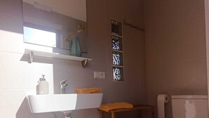 A bathroom with a white sink, a toilet, a small trash bin, and a shelf with toiletries. - Astial Ezquerra Experience – Nature with Charm (Sierra de la Demanda)