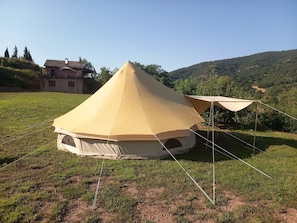 Una tienda de forma cónica en un campo cubierto de hierba, con una casa al fondo.