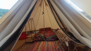 A tent with a bed, a hanging light, and a colorful striped carpet. - Astial Ezquerra Experience – Nature with Charm (Sierra de la Demanda)