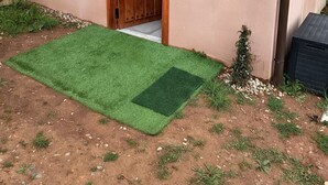A house with a wooden door, a small garden area with artificial grass, and a metal railing on the balcony. - Astial Ezquerra Experience – Nature with Charm (Sierra de la Demanda)