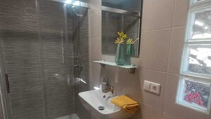 Un baño moderno con cabina de ducha de vidrio, un lavabo con espejo y un perchero con una toalla amarilla.