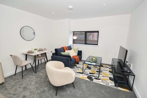 Uma sala de estar moderna com sofá, mesa de jantar, cadeira, televisão e janela com persianas.