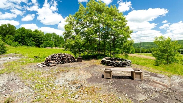 A rustic outdoor setting with a pile of firewood, a stone fire pit, and a wooden bench. - Serene Getaway on Private Land with Panoramic Views in Walton, New York (Walton)