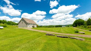 A large barn with a sloped roof, surrounded by a well-maintained grassy field and a dirt path leading to it. - Serene Getaway on Private Land with Panoramic Views in Walton, New York (Walton)