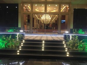 L’entrée d’un hôtel, avec un grand escalier, un lustre et une façade en verre.