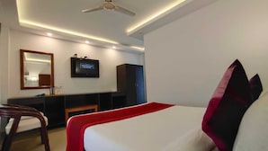 Habitación de hotel con cama, escritorio, silla, televisor y ventilador de techo.
