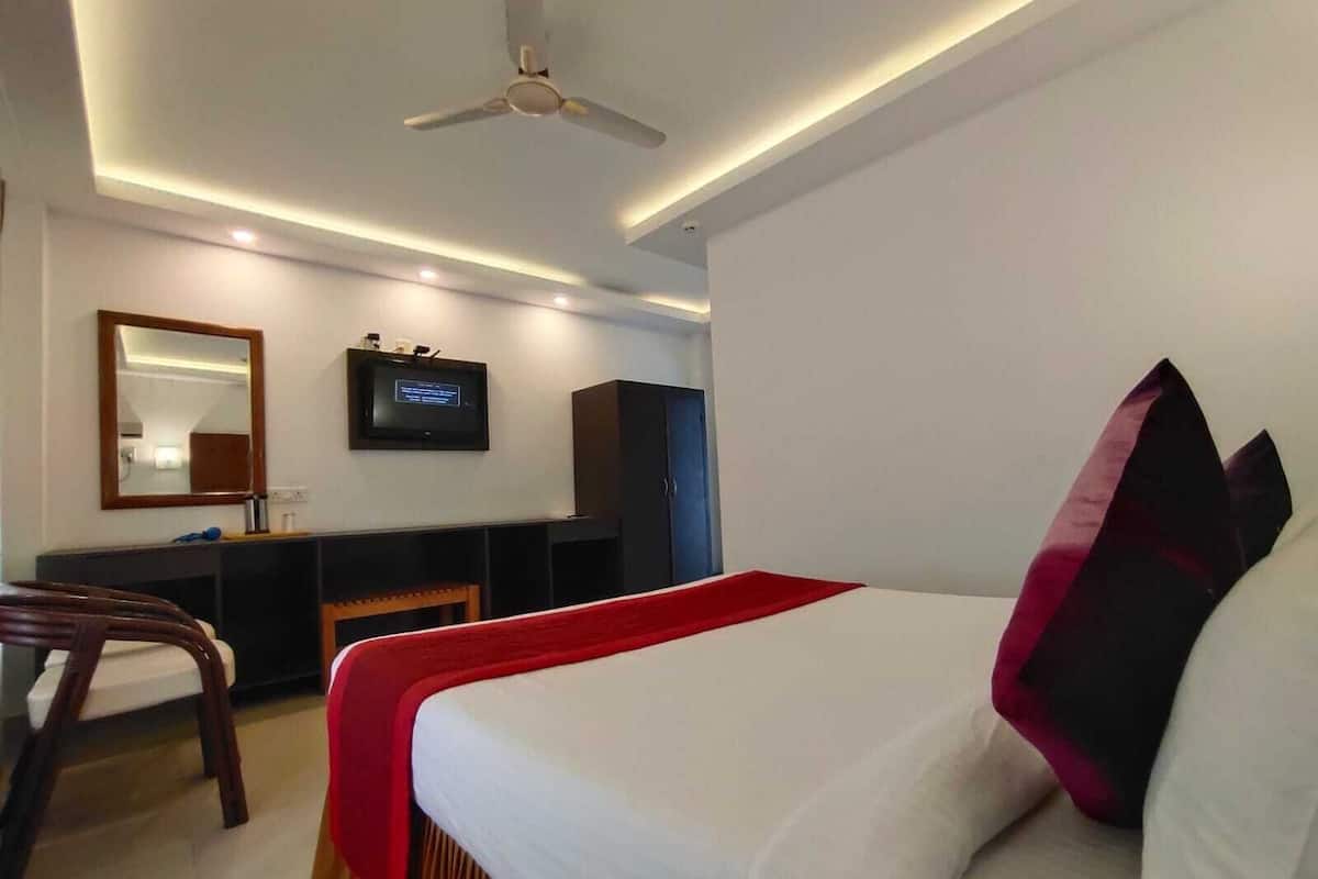 A hotel room with a bed, a desk, a chair, a television, and a ceiling fan.