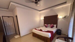 Habitación de hotel con cama, una silla, un ventilador de techo, una puerta y una lámpara fijada a la pared.