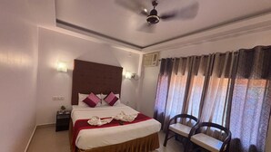 Una habitación de hotel con una cama, una mesita de noche, una silla, un ventilador de techo y una ventana con cortinas.