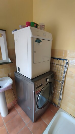 Un espace réduit dédié à la buanderie, comprenant une machine à laver et un sèche-linge superposés, un évier et un étendoir métallique.