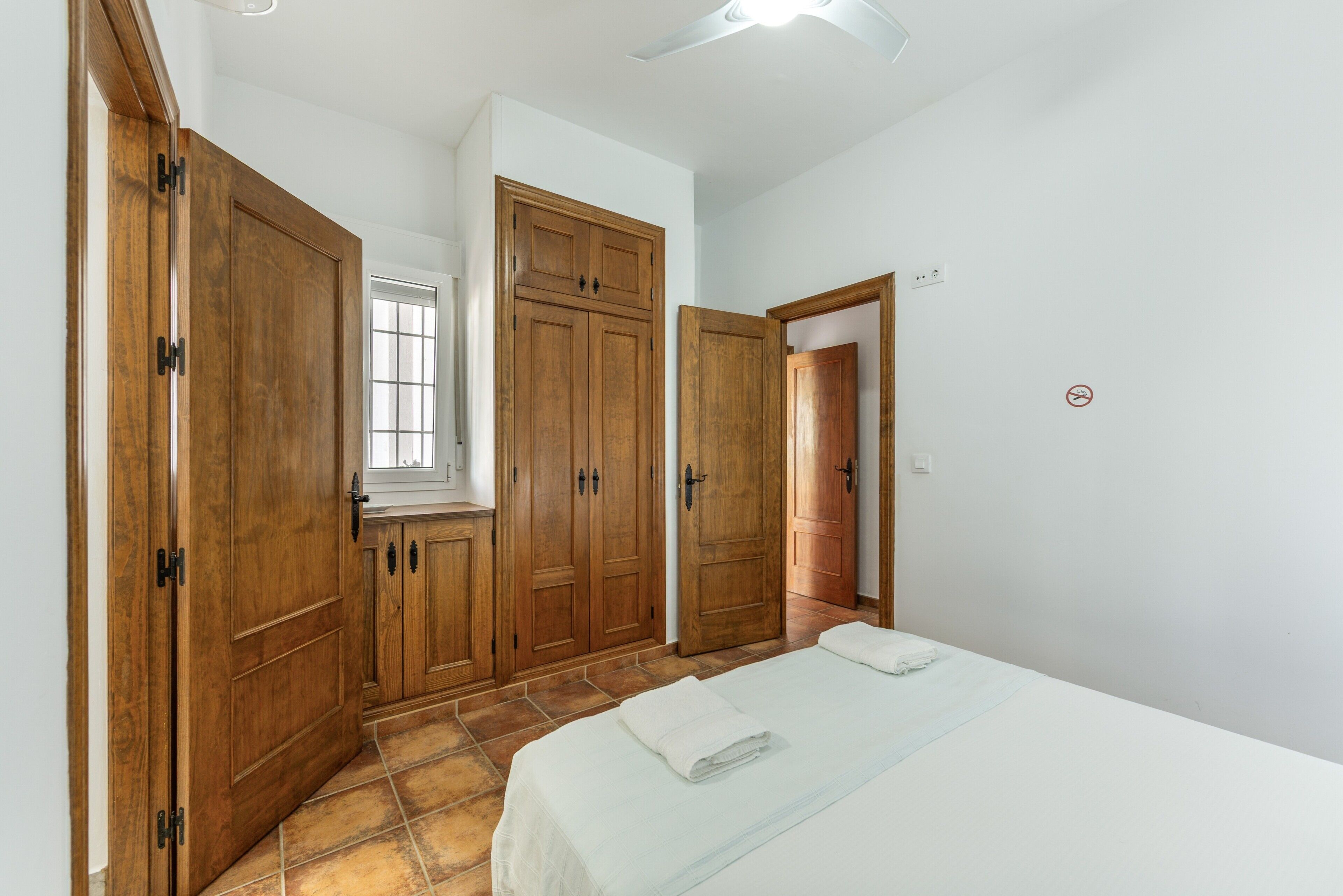 Een slaapkamer met een bed, houten kasten, een raam en een plafondventilator.