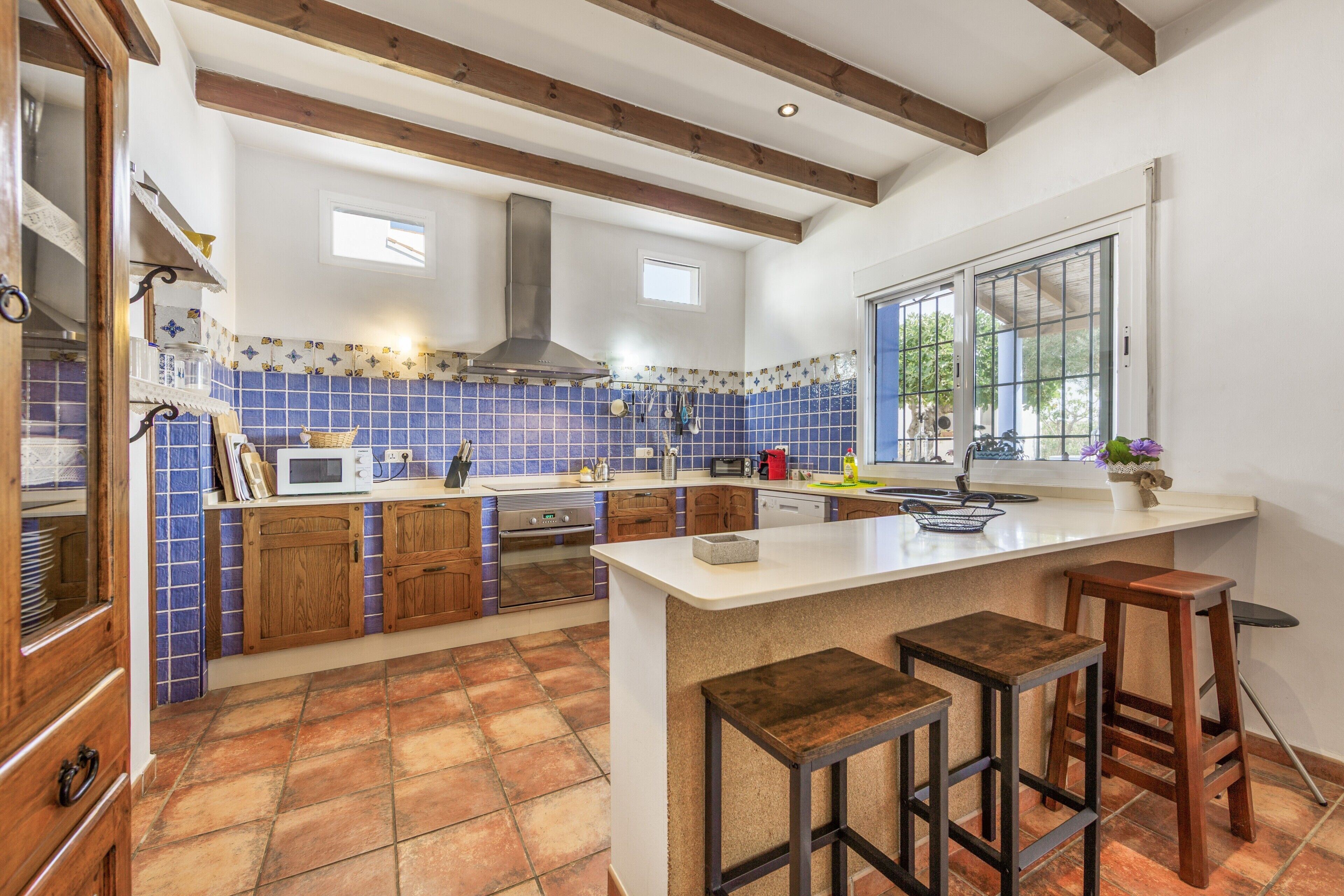 A kitchen with wooden cabinets, a central island with stools, a window, and a tiled backsplash.