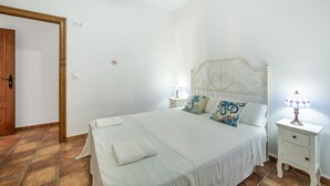 A bedroom with a bed, two bedside tables, a nightstand, a wooden door, and a tiled floor. - My Grandparents’ Country House (Los Gallardos)