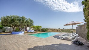 A swimming pool with lounge chairs and an umbrella, surrounded by a wooden deck and a stone wall. - My Grandparents’ Country House (Los Gallardos)