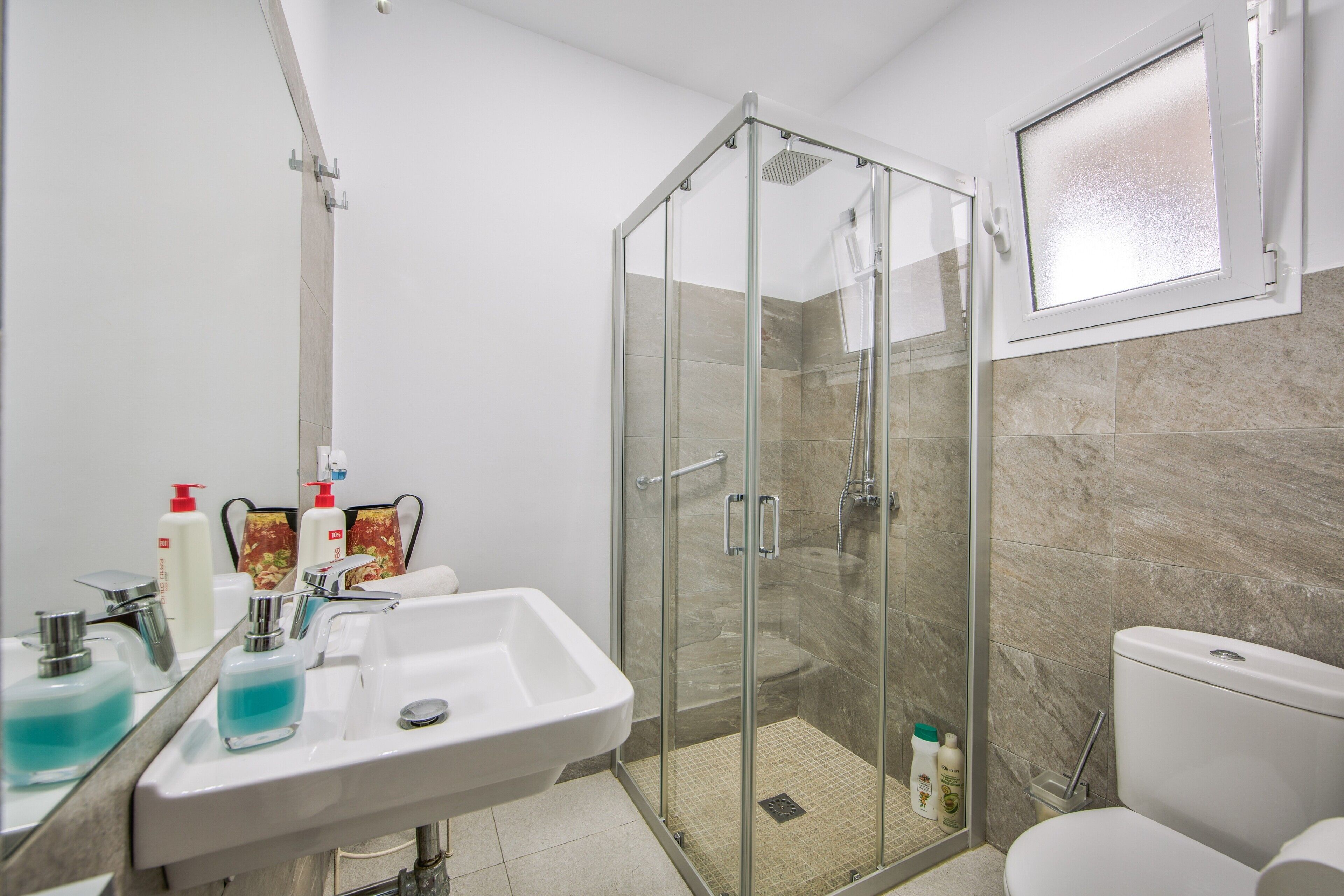 Un baño moderno con ducha de vidrio, lavamanos con dispensadores de jabón y un inodoro.