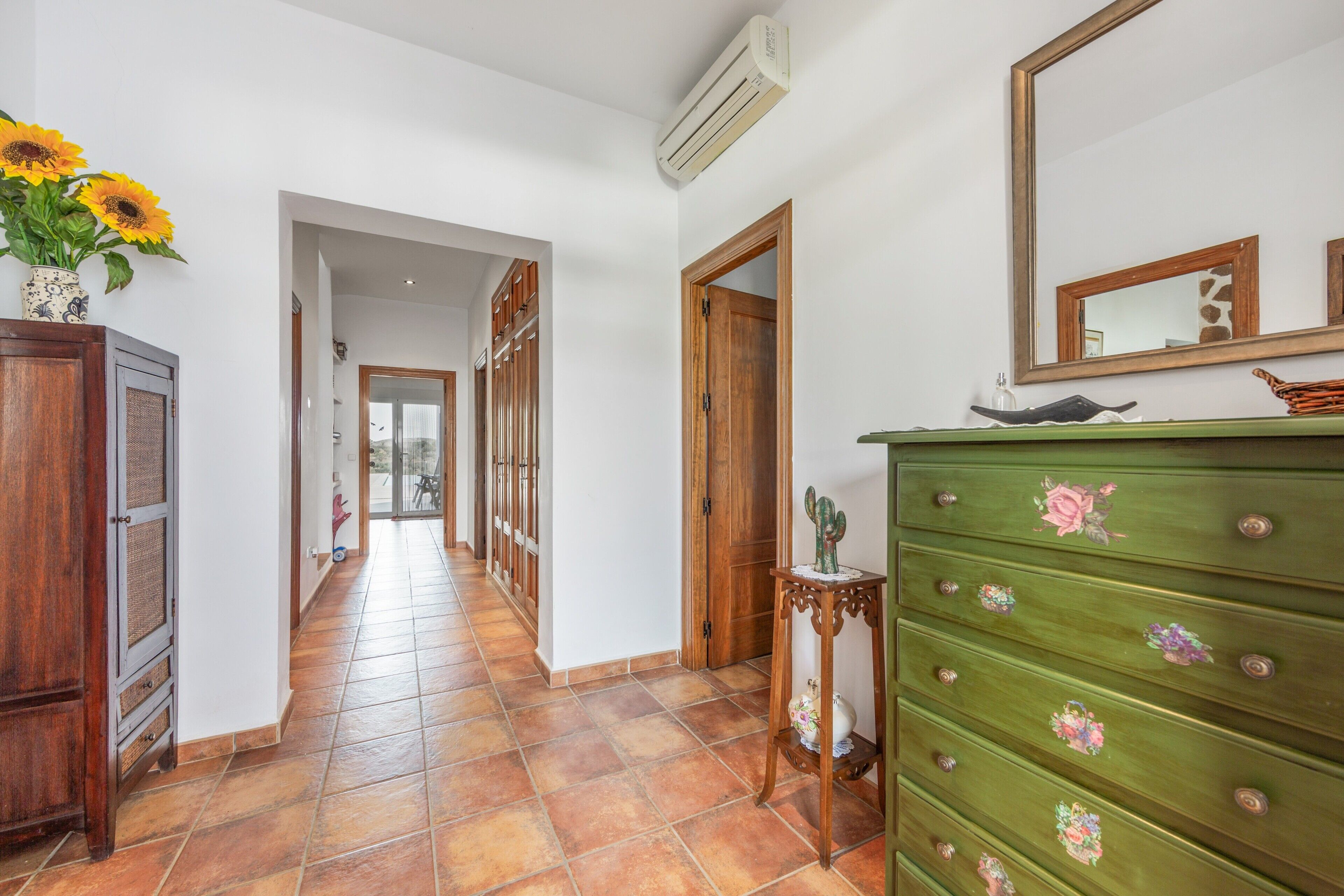 A hallway with a wooden cabinet, a dresser with floral decorations, and a mirror on the wall.