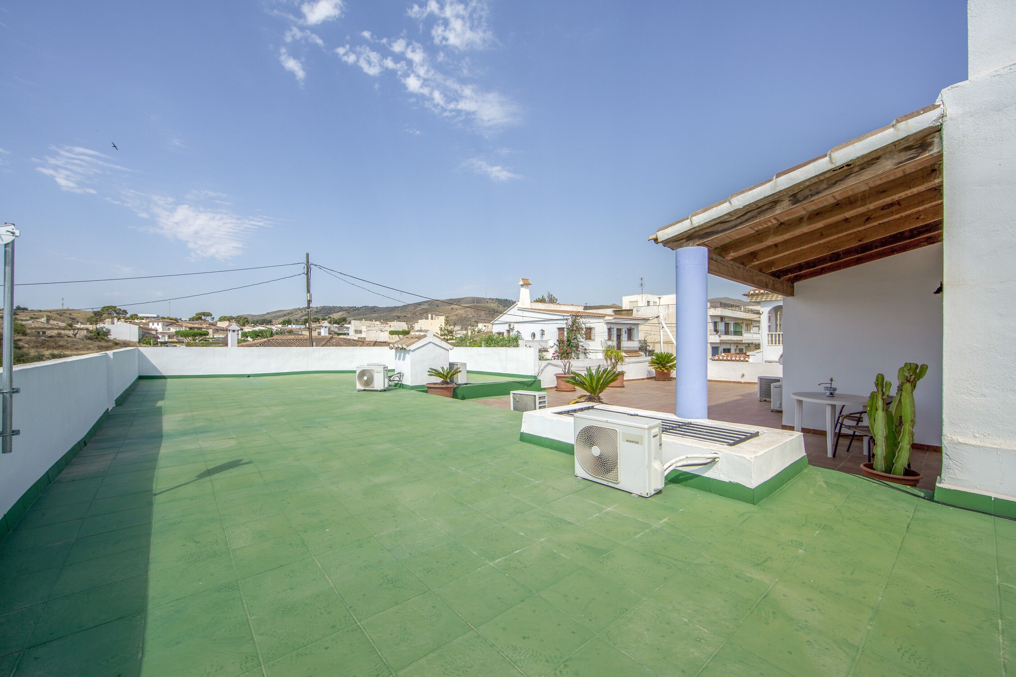 Terraço no telhado com piso verde, mobiliário de exterior, plantas em vasos e vista para edifícios distantes.