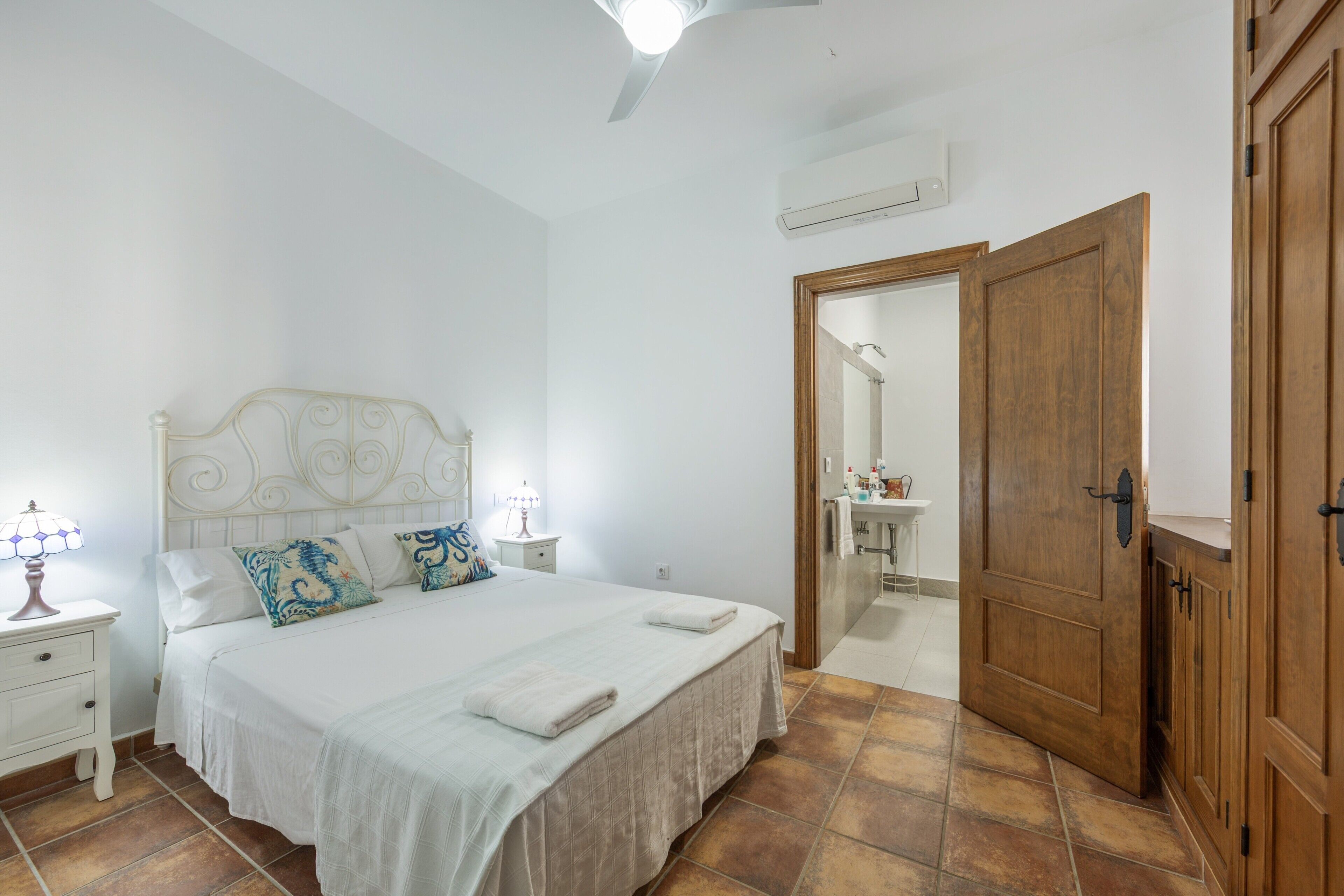Une chambre à coucher comprenant un lit, une table de chevet, une lampe et une porte en bois donnant sur une salle de bain.