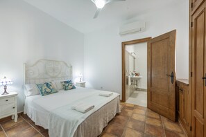 Un dormitori amb un llit, una tauleta de nit, una làmpada i una porta de fusta que dona a un bany.
