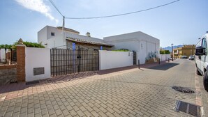 A paved street leading to a gated white building with a tiled roof, a parked vehicle, and a clear sky. - My Grandparents’ Country House (Los Gallardos)