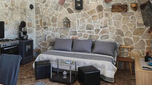 Ein Zimmer mit Steinwänden, einem Bett, einer Kaffeemaschine, einem Herd und einem Holzschild.