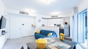 Een moderne keuken met witte kastjes, een blauwe bank en een eethoek met een tafel voor twee personen.
