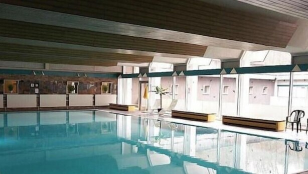 Ein Hallenbad mit Holzbalkendecke, einer Sitzbank am Beckenrand und Blick ins Becken.