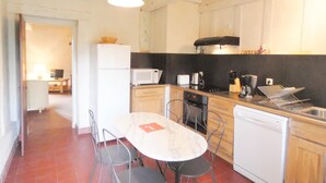 Kompakti keittiö, jossa on valkoiset kaapit, mikroaaltouuni, liesi ja pesuallas. Keittiössä on myös ruokapöytä ja tuolit.