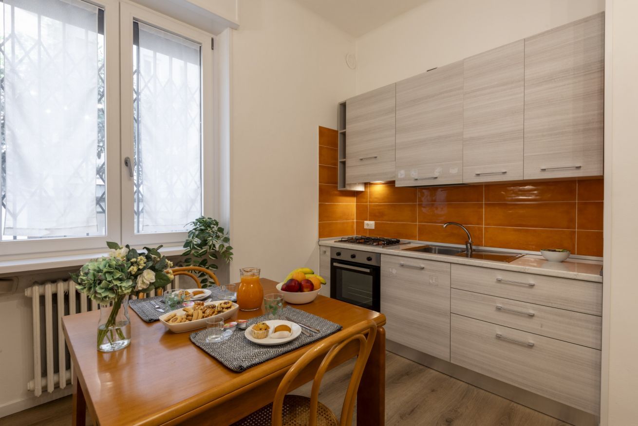 A modern kitchen with white cabinets, a sink, and a dining area with a table set for breakfast.