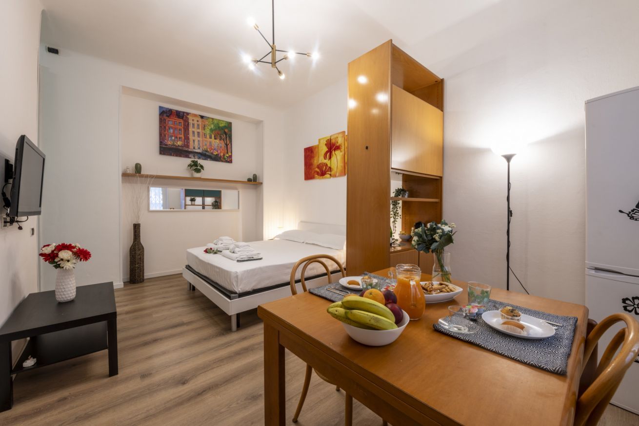 Una habitación de hotel funcional con cama, una mesa para desayunar, televisión y obras de arte en las paredes.
