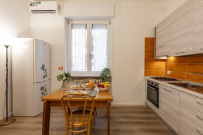 Eine kompakte Küche mit Esstisch, gedecktem Frühstückstisch, Kühlschrank und einem Fenster mit Jalousien.