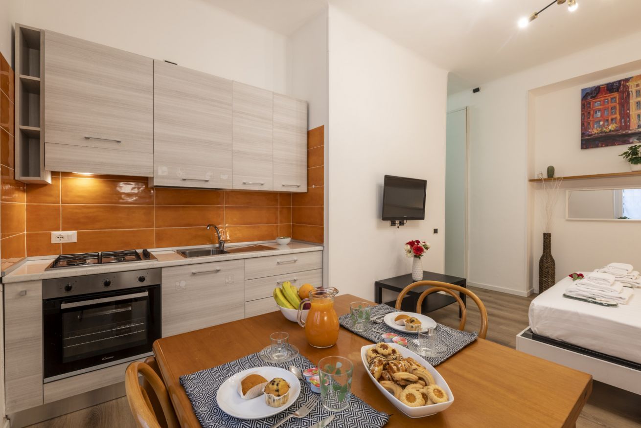 A modern kitchen with a dining area, a TV, and a bed with towels.