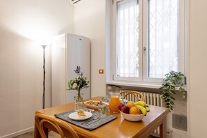 Ein Essbereich mit einem für das Frühstück gedeckten Tisch, einem Heizkörper, einem Fenster mit Jalousien und einer Pflanze.