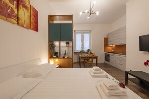 Ein Schlafzimmer mit Bett, Schreibtisch, Esstisch und einer Küchenzeile.