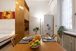 Ein Essbereich mit einem Holztisch, Stühlen, einer Obstschale und einem weißen Kühlschrank.