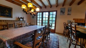 A dining area with a long table, chairs, a chandelier, and a view through a large window. - Charming country house between the forest and the ocean - Contis (Lit-et-Mixe)