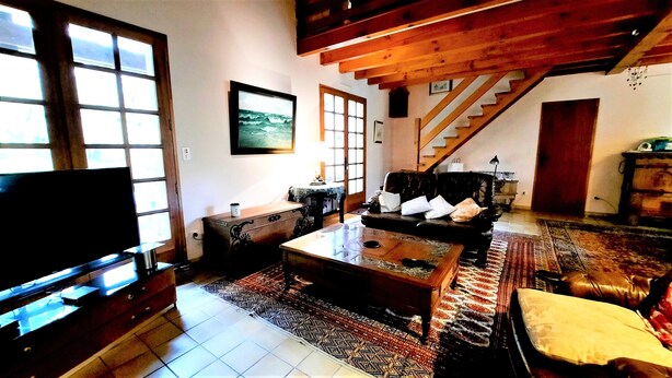 A living room with a sofa, a coffee table, a TV, a staircase, and a patterned rug. - Charming country house between the forest and the ocean - Contis (Lit-et-Mixe)