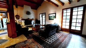 A living room with a fireplace, a sofa, a television, and a large window. - Charming country house between the forest and the ocean - Contis (Lit-et-Mixe)