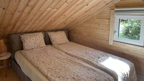 A bedroom with a sloped ceiling, a bed with floral bedding, a window with a view, and a small table with a lamp. - Log cabin with hot tub and views (Bondemölla)