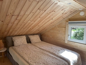 Ein Schlafzimmer mit schrägen Wänden, einem Bett mit Blumenmuster-Bettwäsche, einem Fenster mit Aussicht und einem kleinen Tisch mit Lampe.