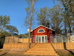 A red building with a wooden staircase leading to a glass door, surrounded by trees.