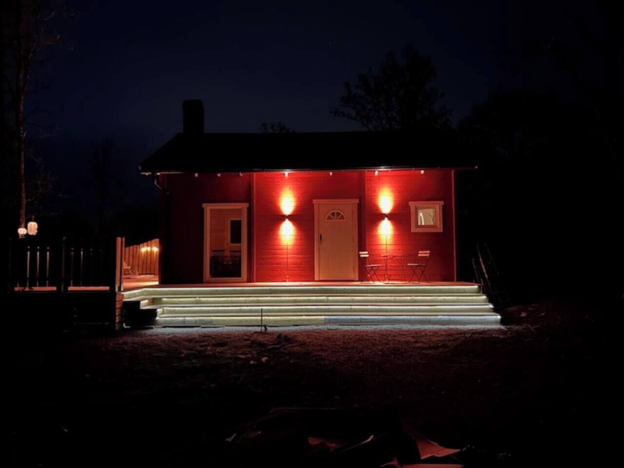 A red building with a front porch, steps, and two illuminated wall sconces.