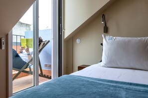 Quarto com cama, mesa de cabeceira, luminária na parede e vista pela janela.