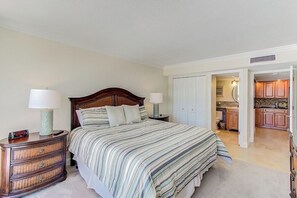 A bedroom with a bed, nightstands, and a dresser. There is a door leading to a bathroom and a kitchen. - Unit 97- 2 Bedroom and 2 Bathroom Condominium with Partial South Views. (Sarasota)