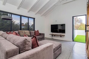 Un salon moderne avec un grand canapé d’angle, un téléviseur à écran plat fixé sur une étagère en bois et une lucarne au-dessus.