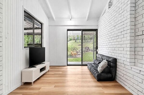 A modern living room with a TV, a sofa, and a sliding glass door leading to a garden. - Arielle’s haven (Cedar Creek)