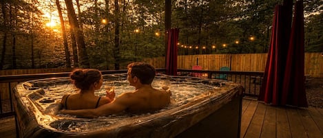 A hot tub with two people, surrounded by a wooden deck and trees, with string lights in the background.