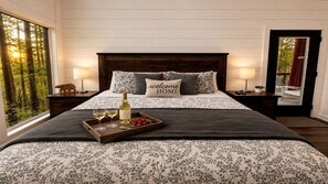 Ein Schlafzimmer mit einem großen Bett, zwei Nachttischlampen, einem Tablett mit Weingläsern und Erdbeeren sowie einem 'welcome home'-Kissen.