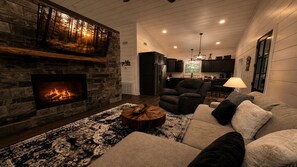 Ein gemütliches Wohnzimmer mit Kamin aus Stein, einer Couch, einem Couchtisch und einer Küche im Hintergrund.