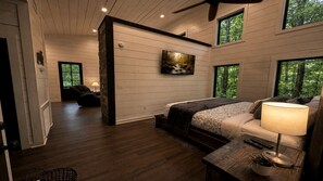 Ein Schlafzimmer mit einem Bett, einem Nachttisch, einer Lampe, einem Gemälde und Blick ins Freie durch Fenster.